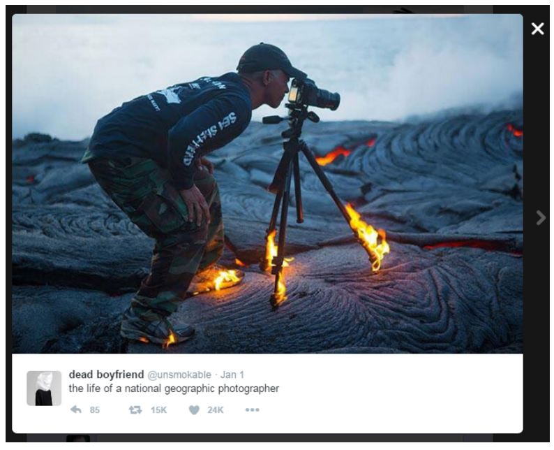 A tweet by @unsmokable that reads “the life of a national geographic photographer” and shows a photo of a man standing on volcanic terrain and looking through a camera situated on a tripod. The photographer’s shoes and tripod have flames around them.